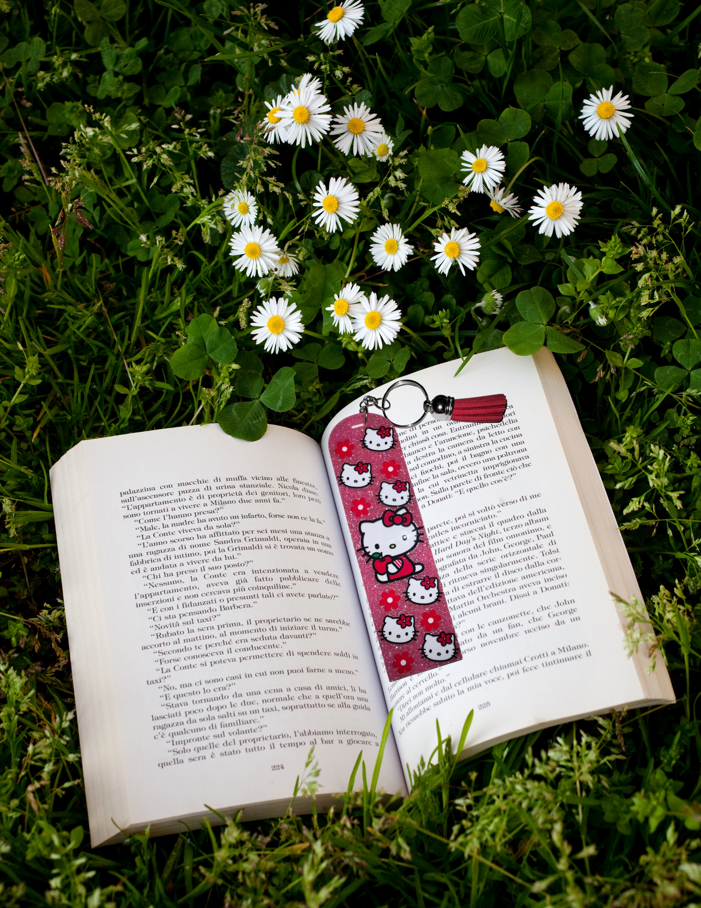 Acrylic bookmark with cute cat design on open book amidst flowers and grass.