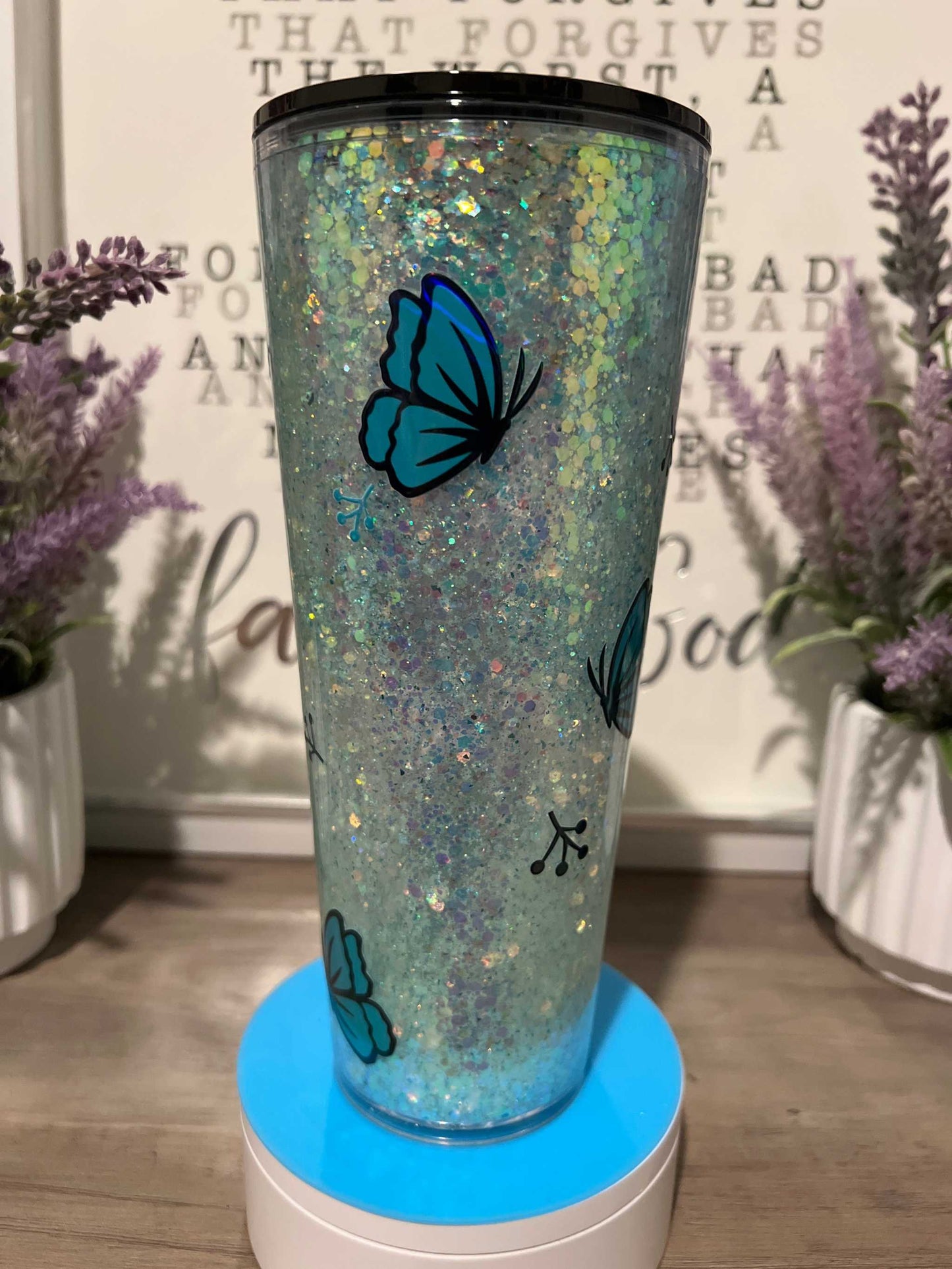 Blue butterfly-themed glitter tumbler with floral background.