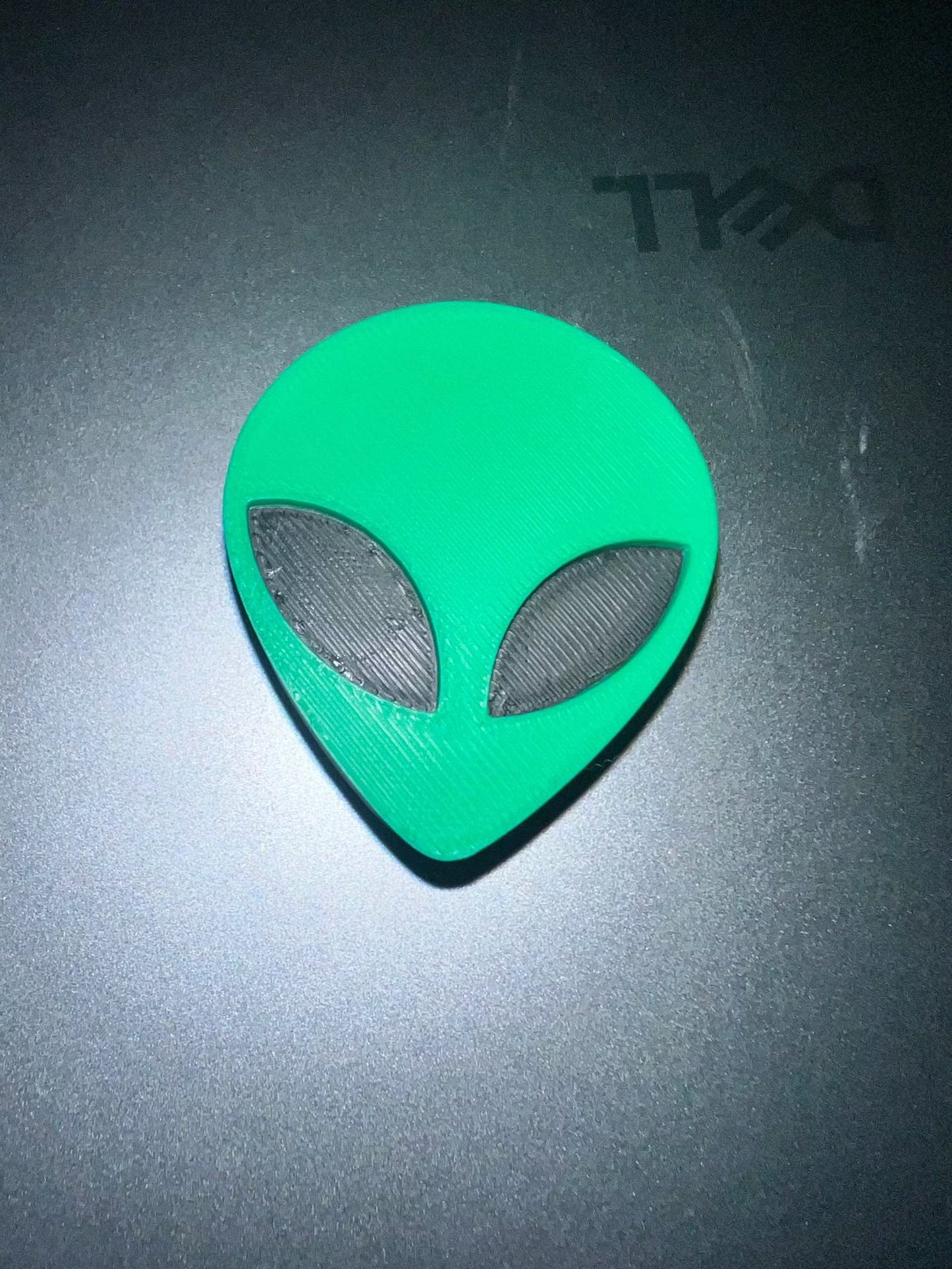 Alien head straw topper in green with black eyes on dark surface