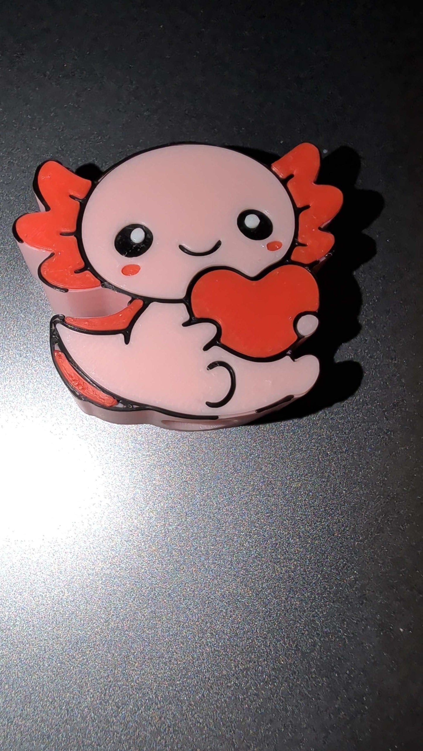 Cute pink axolotl straw topper holding a red heart with orange gills on a dark background
