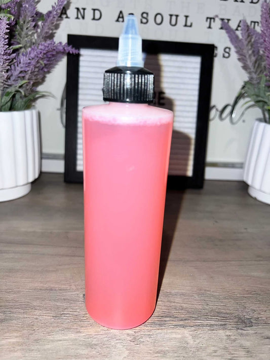 Pink squeeze bottle with black and blue nozzle on wooden table.
