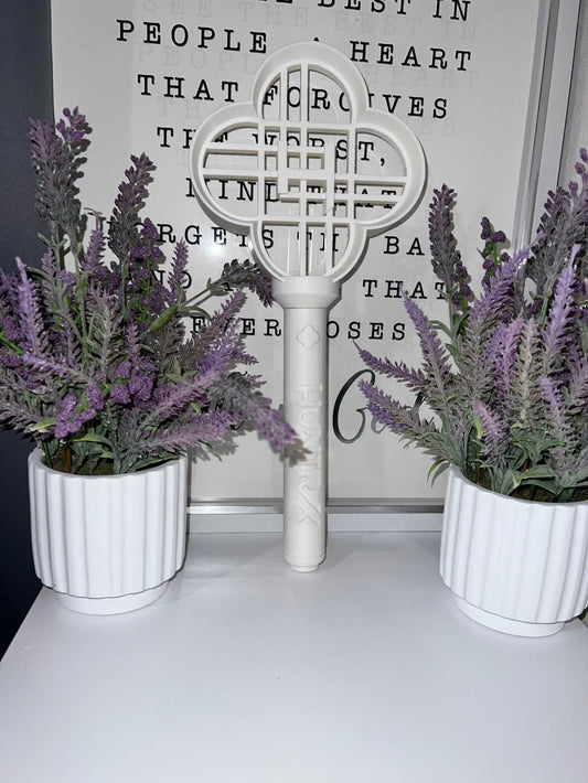 White Huntrix Cosplay wand standing between two lavender plants in white pots on a white surface with a text background