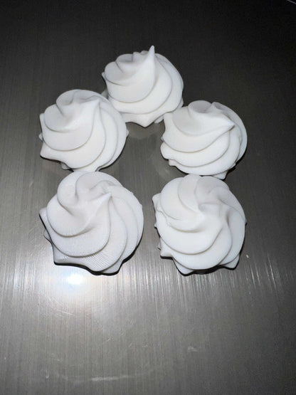 Five white whipped cream lid toppers arranged on a gray surface for decorative use on drink lids.