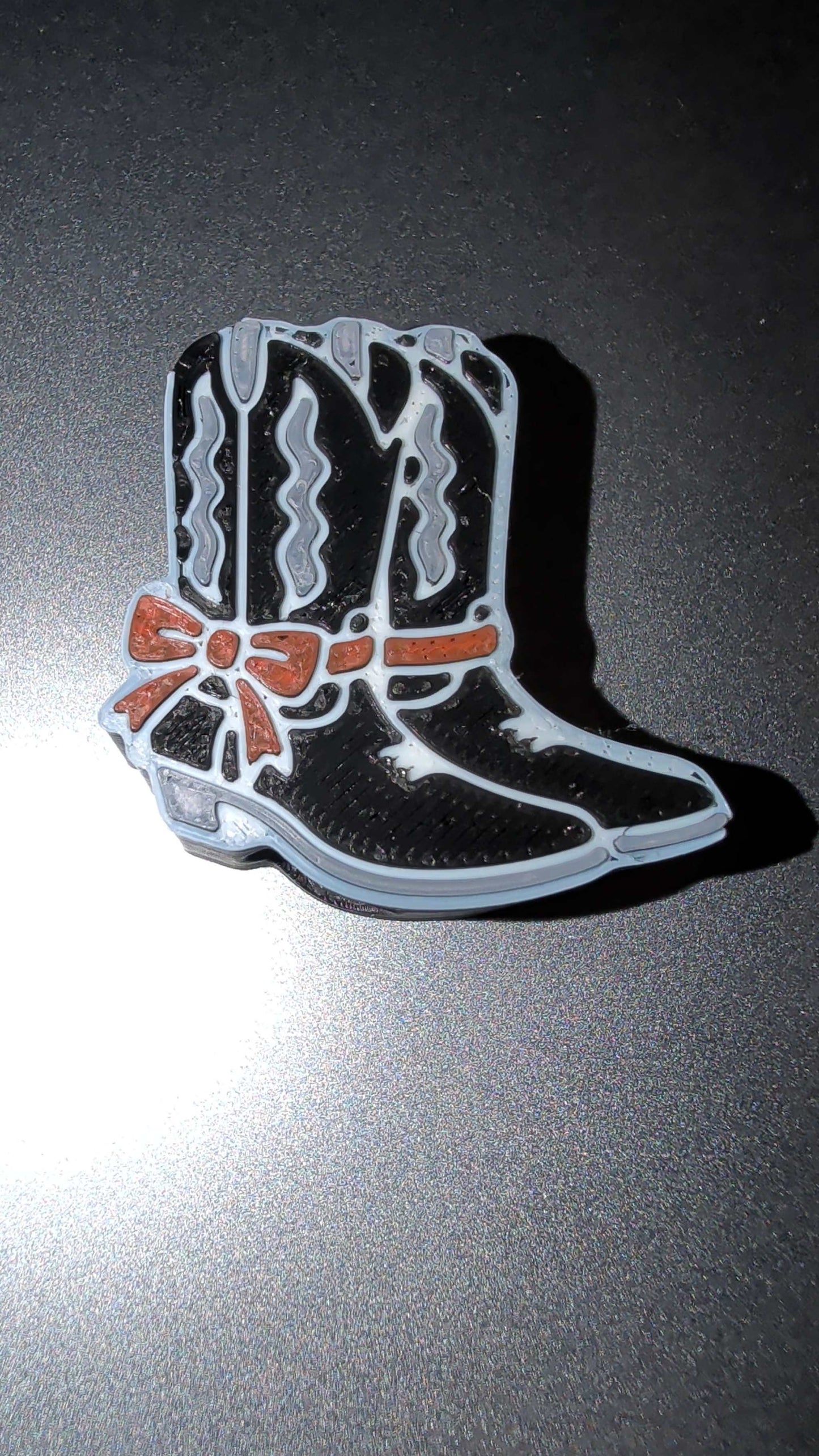 Black and white country boots pin with red bow detail on dark background