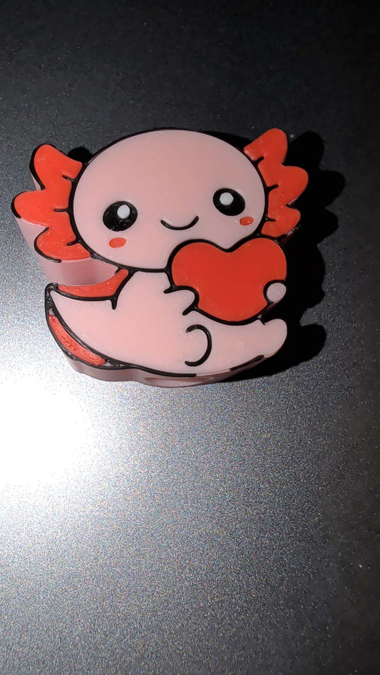 Cute pink axolotl straw topper holding a red heart with orange gills on a dark background