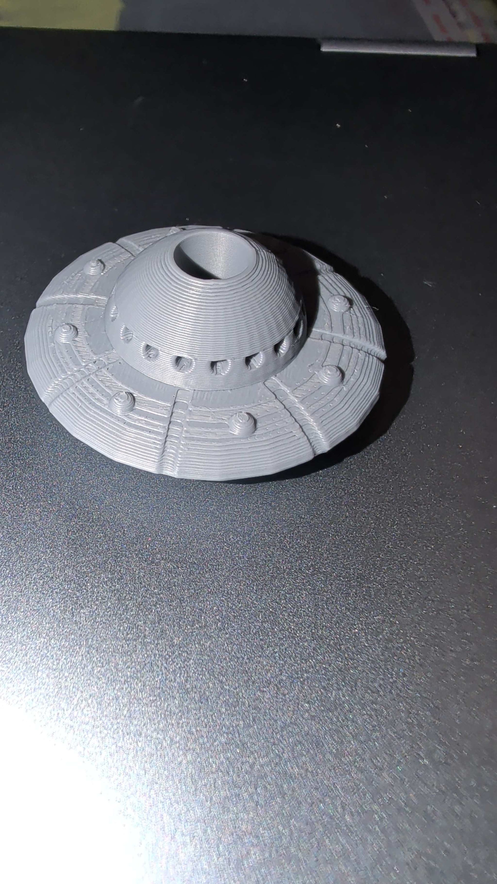 Gray 3D printed space ship straw topper on dark surface